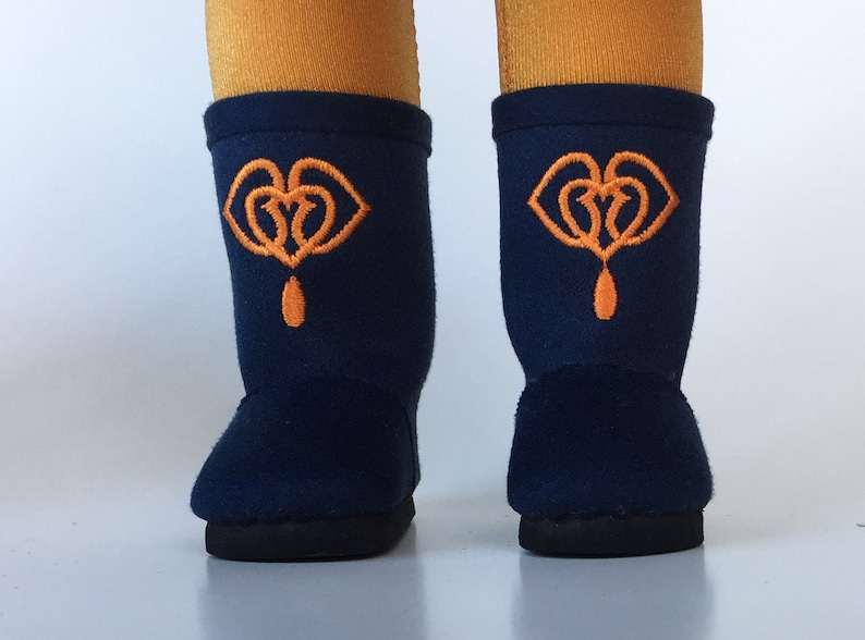 Puede incluir: Un par de botas de forro polar azul oscuro con corazones bordados en naranja y un dise&ntilde;o de l&aacute;grima.