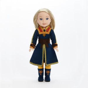 Puede incluir: Una mu&ntilde;eca con un vestido azul y dorado con un cintur&oacute;n marr&oacute;n. La mu&ntilde;eca tiene el pelo rubio y los ojos azules.
