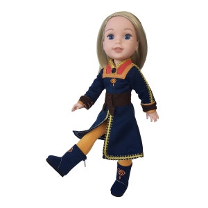 Puede incluir: Una mu&ntilde;eca con un atuendo azul y dorado con un cintur&oacute;n marr&oacute;n. La mu&ntilde;eca tiene el pelo rubio y los ojos azules.
