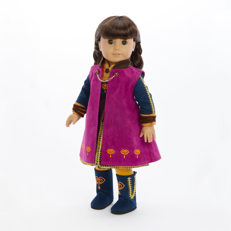 May include: A doll wearing a purple and blue dress with gold accents and matching boots. The doll has brown hair and brown eyes.