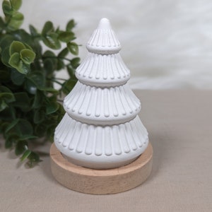 May include: A white ceramic Christmas tree with a wooden base. The tree has three tiers with a fluted design.
