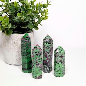 May include: Four green and pink gemstone points, also known as ruby zoisite, arranged on a white surface. The points are polished and have a natural, striated appearance.