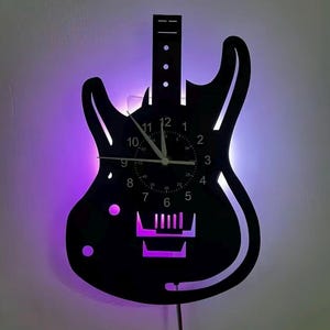 May include: A black wall clock shaped like an electric guitar with a purple LED backlight. The clock face features white numbers from 1 to 12, smaller minute markers, and white hour, minute, and second hands. The guitar body has cutouts.