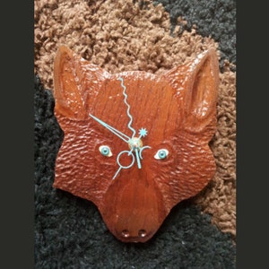 May include: A wooden wall clock carved in the shape of a wolf's head. The clock has blue hands and blue eyes.