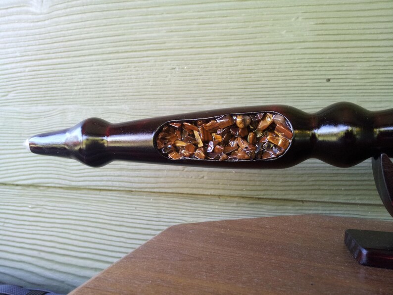 Puede incluir: Una pipa de madera marr&oacute;n oscuro con una secci&oacute;n ahuecada llena de peque&ntilde;as piedras de color &aacute;mbar. La pipa tiene un acabado liso y brillante y est&aacute; sobre una superficie de madera. Dise&ntilde;o &uacute;nico y artesanal.