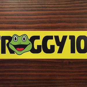 May include: A yellow banner with black text that reads "FROGGY 101". A green frog with red mouth and black eyes is centered in the text.