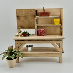 May include: A miniature wooden potting bench with a pegboard back, shelves, and a lower shelf. It features a small red basket, a yellow pot, and a red and white patterned pot. A potted plant and a small metal bucket are also present.