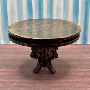 May include: A dark brown wooden table with a round top and a carved base. The table is made of wood and has a rustic look.