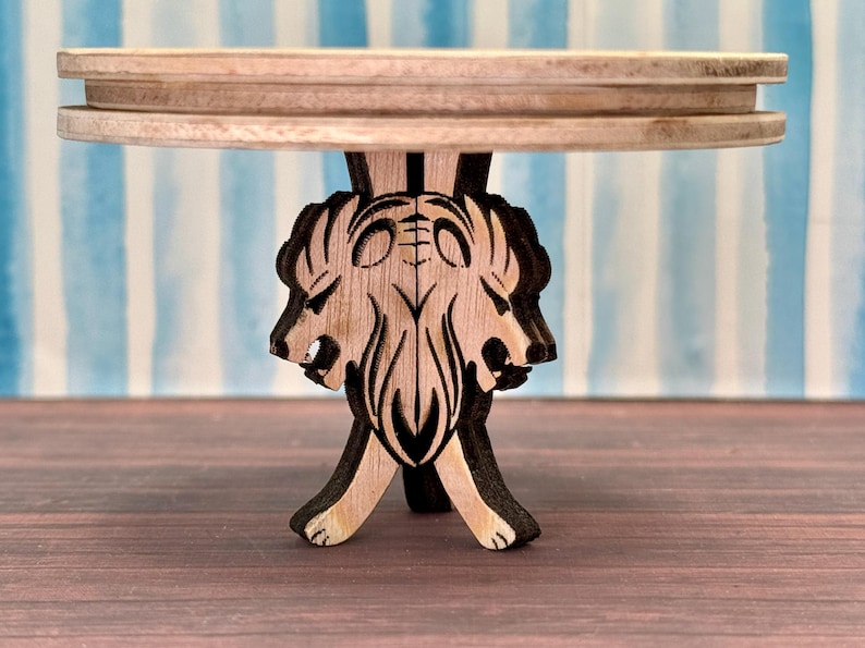May include: A wooden table with a round top and a base carved in the shape of three lion heads. The table is made of light brown wood and has a natural finish.