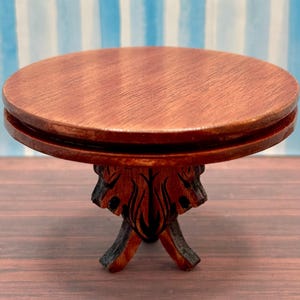 May include: A small, round, wooden table with a dark brown finish. The table has a carved base with a floral design.