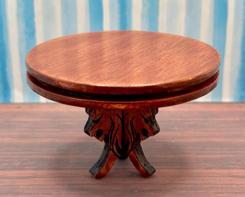 May include: A small, round, wooden table with a dark brown finish. The table has a carved base with a floral design.