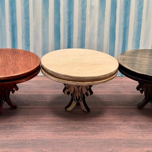 May include: Three round wooden tables with carved legs. The tables are in different shades of brown, including a dark brown, a light brown, and a reddish brown.