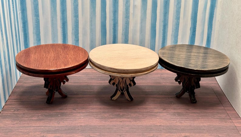 May include: Three round wooden tables with carved legs. The tables are in different shades of brown, including a dark brown, a light brown, and a reddish brown.