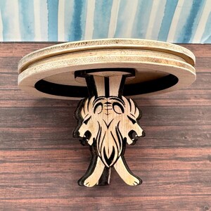 May include: A wooden table with a round top and three legs shaped like lion heads. The table is made of light wood and has a dark brown stain.