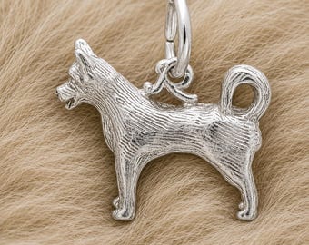 May include: A silver-toned metal charm shaped like a standing dog with pointed ears and a curled tail. The surface features etched lines to represent fur texture. A circular jump ring is attached to the top of the dog's back for hanging.