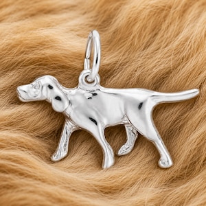May include: A polished silver-toned metal charm shaped like a hunting dog in a standing profile position. The charm features a smooth, reflective surface and includes a circular jump ring attached to the top for hanging or attaching to a chain.