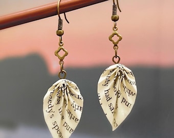 May include: A pair of earrings with bronze-colored hooks and charms. Each earring features a leaf-shaped charm made from folded pages of a book. The text on the pages is visible.