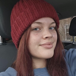 May include: A ribbed, burgundy-colored knit beanie. The hat is made of a soft material and has a classic, close-fitting design. The beanie is a warm and stylish accessory for cold weather.
