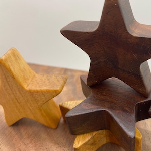 May include: Wooden star-shaped objects in varying shades of brown and tan are arranged on a wooden surface. The stars are stacked and arranged to create a decorative display. The wood grain is visible.