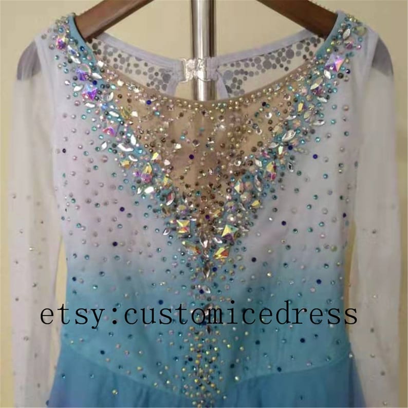 May include: A light blue figure skating dress with long sleeves and a V-neckline. The dress is decorated with iridescent rhinestones and has a gradient design. The text "etsy: customicedress" is visible at the bottom of the dress.