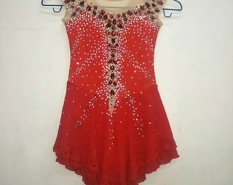 May include: Red figure skating dress with a sheer mesh neckline and a beaded design. The dress has a layered skirt and is decorated with rhinestones.