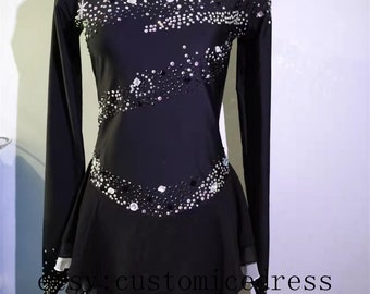 Op de afbeelding: Zwarte kunstschaatsjurk met lange mouwen en een witte chiffonrok. De jurk is versierd met strass in een sterren- en golfpatroon.