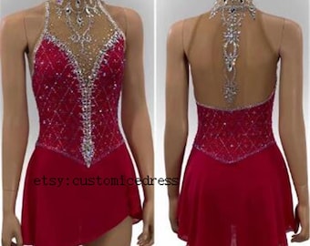 May include: A red figure skating dress with a high neckline and a sheer panel in the front. The dress is decorated with rhinestones and has a skirt that is slightly shorter in the front than in the back. The dress is shown on a mannequin.