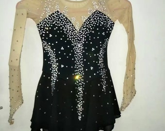 Op de afbeelding: Een zwarte kunstschaatsjurk met lange mouwen en een transparante mesh overlay. De jurk is versierd met strass steentjes en heeft een sweetheart halslijn.