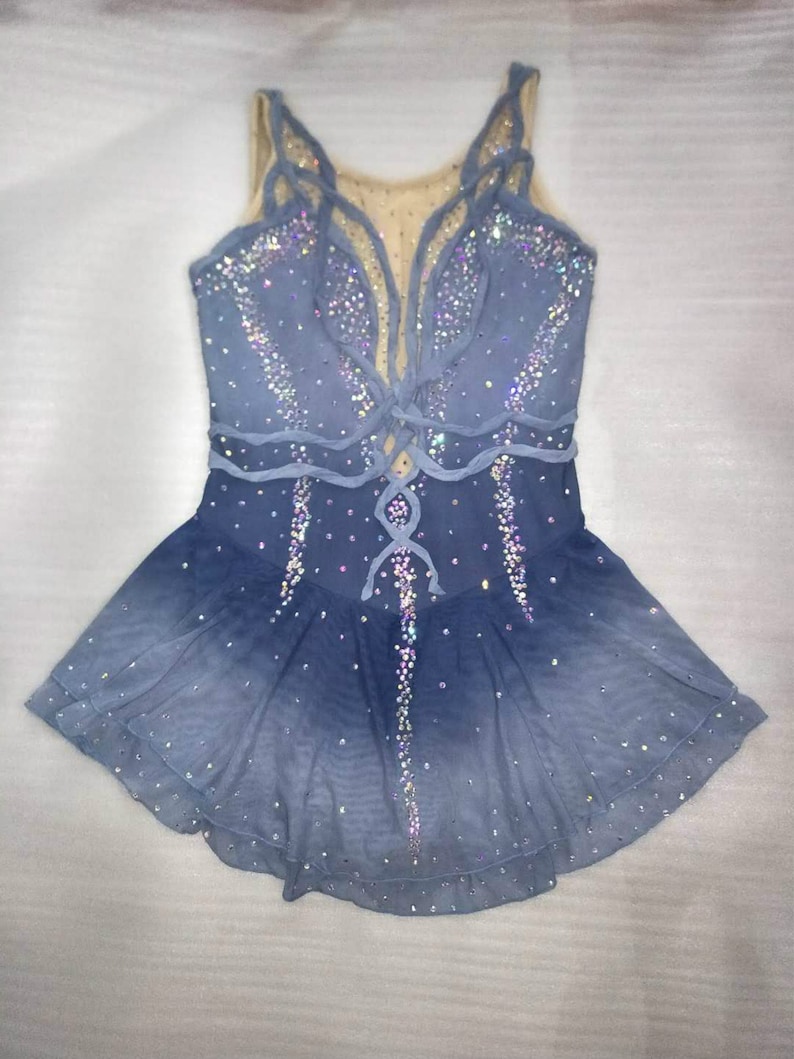 May include: A blue figure skating dress with a lace-up bodice and a layered skirt. The dress is decorated with iridescent rhinestones.