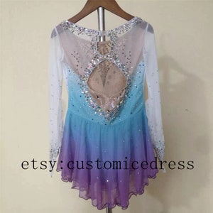 May include: A long-sleeved ice skating dress with a gradient design in shades of blue and purple. The dress has a sheer back with a rhinestone design and a keyhole opening. The dress is on a hanger and has the text "etsy: customicedress" at the bottom.