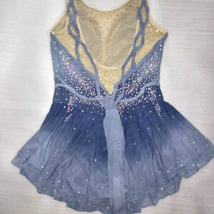 May include: A blue and white figure skating dress with a mesh bodice and a layered skirt. The dress is decorated with rhinestones and has a criss-cross back design.