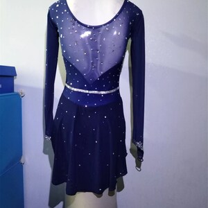 Puede incluir: Un vestido de patinaje art&iacute;stico azul marino con mangas largas y un panel trasero de malla transparente. El vestido est&aacute; decorado con diamantes de imitaci&oacute;n y un cintur&oacute;n de diamantes de imitaci&oacute;n plateado.