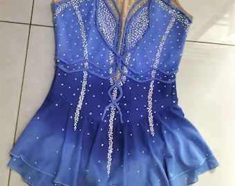 Op de afbeelding: Een blauwe en witte kunstschaatsjurk met een mesh-bovenstuk en een gelaagde rok. De jurk is versierd met strass en heeft een kruisvormig ontwerp op het bovenstuk. De jurk is te koop op Etsy, zoals aangegeven door de tekst "etsy: customicedress" onderaan de afbeelding.