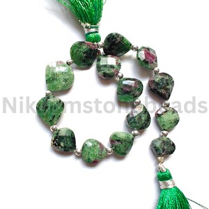Może przedstawiać: Sznur koralik&oacute;w z zielonych i czerwonych kamieni szlachetnych ze srebrnymi akcentami. Koraliki są fasetowane i mają mieszankę zielonych i czerwonych kolor&oacute;w. Sznur jest wykończony zielonymi frędzlami i tekstem "Nikomstonbeads".
