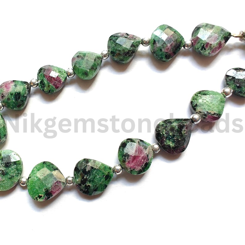 Może przedstawiać: Szereg fasetowanych koralik&oacute;w z kamieni szlachetnych. Koraliki są mieszanką zieleni i czerwieni, ze srebrnymi przekładkami. Kamienie szlachetne mają kształt serca. Tekst "Nikgemstonebeads" jest widoczny na zdjęciu.