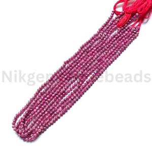 May include: Strands of faceted, deep pink gemstone beads. The beads are strung together with red thread, creating a cascading effect. The image is well-lit, showcasing the beads' color and texture. The beads are likely used for jewelry making.