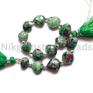 Może przedstawiać: Szczeg&oacute;łowe ujęcie fasetowanych zielonych i czerwonych koralik&oacute;w z kamieni szlachetnych ze srebrnymi przekładkami. Koraliki są nawleczone, tworząc zakrzywiony kształt. Zielone frędzle przymocowane na każdym końcu. Naturalny wygląd.