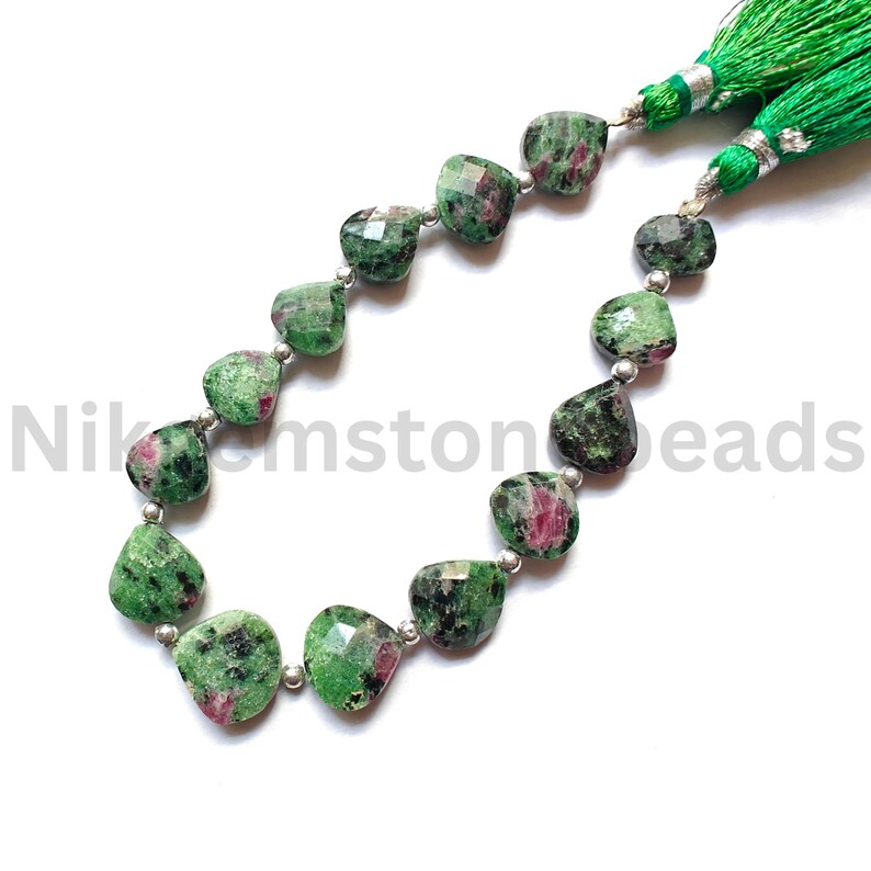 Może przedstawiać: Naszyjnik z zielono-czerwonych koralik&oacute;w z rubinu zoisytu w kształcie serca. Koraliki są nawleczone na srebrny drut. Zielone frędzle ze srebrnymi detalami są przymocowane do końc&oacute;w. Widoczny jest tekst "Nikemstone beads".