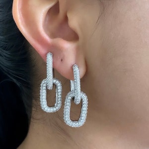 Può includere: Orecchini pendenti in argento con un design a catena a maglie, impreziositi da pietre di zircone cubico trasparenti.