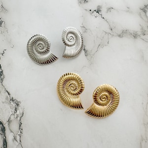 Puede incluir: Un par de pendientes con forma de concha de nautilus. Un par es plateado y el otro es dorado.