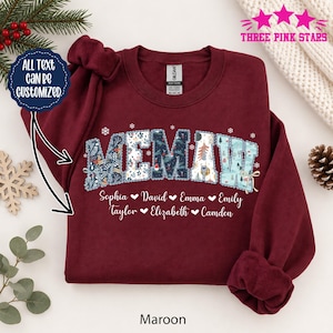 Könnte beinhalten: Ein bordeauxrotes Sweatshirt mit Rundhalsausschnitt, das das Wort MEMAW in einer gemusterten, quiltartigen Schrift mit verschiedenen Winter- und Feiertagsmotiven zeigt. Unter dem Text sind die Namen Sophia, David, Emma, Emily, Taylor, Elizabeth und Camden in Weiß gedruckt.