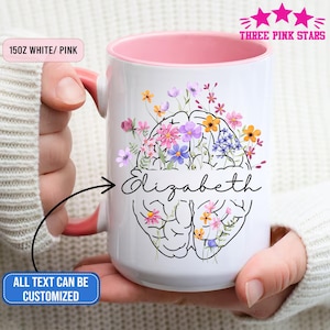Könnte beinhalten: Weiß-rosa Keramikbecher mit einem Fassungsvermögen von ca. 425 ml. Er zeigt ein florales Gehirndesign und den Namen "Elizabeth". Der Becher hat eine rosa Innenseite und einen Griff. Der Text "ALL TEXT CAN BE CUSTOMIZED" steht auf einem blauen Banner.
