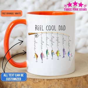 Op de afbeelding: Witte keramische mok met een oranje binnenkant en handvat. De mok heeft de tekst "REEL COOL DAD" met een hengelontwerp en de namen Olivia, Victoria, David, Taylor, Sophie, Alex en Liam. De mok is 312 gram.