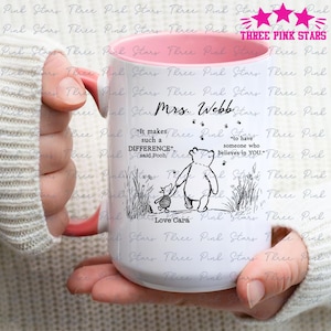 May include: White ceramic mug with a pink interior, featuring a Winnie the Pooh illustration and the quote "It makes such a DIFFERENCE" and "to have someone who believes in YOU." The mug is held by a person.