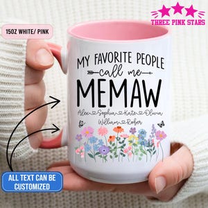 Könnte beinhalten: Eine weiße Keramiktasse mit rosa Innenraum und Griff. Die Tasse trägt den schwarzen Text "MY FAVORITE PEOPLE call me MEMAW" mit Namen darunter. Ein Blumendesign mit Schmetterlingen verziert den Boden. Die Tasse ist 425 ml.