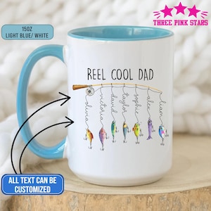 Op de afbeelding: Een witte keramische mok met een lichtblauwe handgreep en binnenkant. De mok heeft de tekst "REEL COOL DAD" met gepersonaliseerde namen die aan een hengel hangen. De mok is ongeveer 425 ml en de tekst "ALL TEXT CAN BE CUSTOMIZED" is ook zichtbaar.