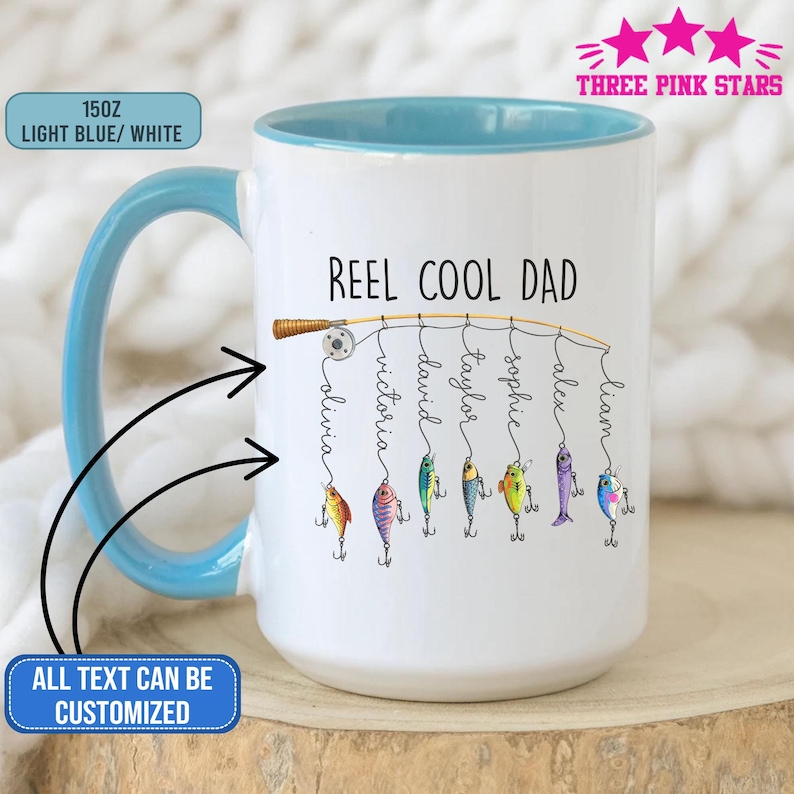 Op de afbeelding: Een witte keramische mok met een lichtblauwe handgreep en binnenkant. De mok heeft de tekst "REEL COOL DAD" met gepersonaliseerde namen die aan een hengel hangen. De mok is ongeveer 425 ml en de tekst "ALL TEXT CAN BE CUSTOMIZED" is ook zichtbaar.