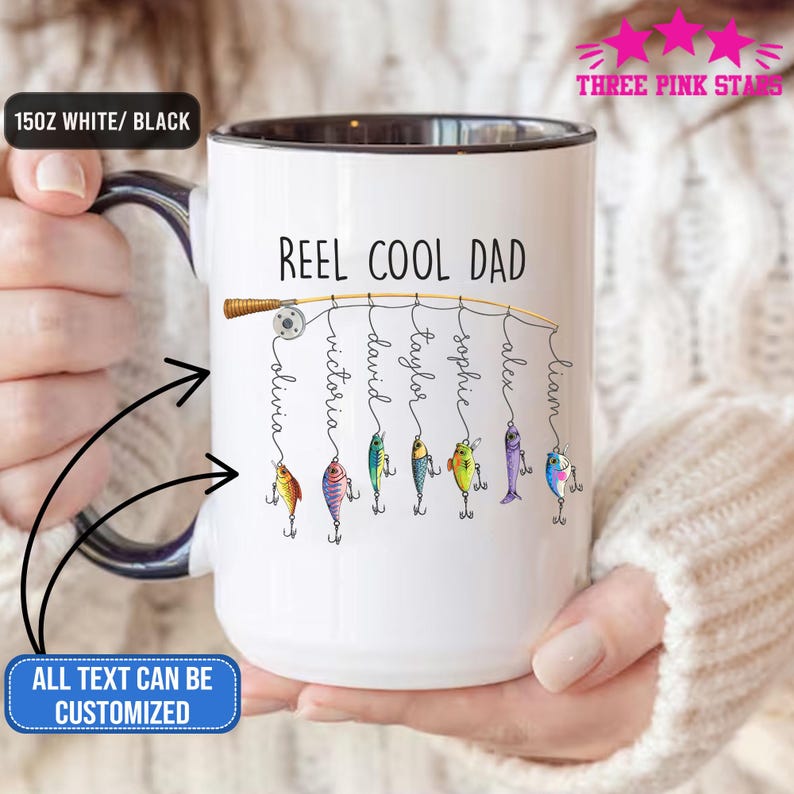 Op de afbeelding: Witte keramische mok met een zwarte binnenkant en handvat. De mok heeft de tekst "REEL COOL DAD" met gepersonaliseerde namen die aan een vislijn hangen. De tekst "ALL TEXT CAN BE CUSTOMIZED" is ook zichtbaar.