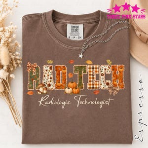 May include: An espresso-colored short-sleeve t-shirt featuring the text RAD TECH and Radiologic Technologist. The letters are decorated with autumn-themed patterns including pumpkins, mushrooms, plaid, and bows, accented by falling leaves.
