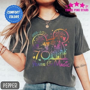 May include: Dark gray t-shirt with a colorful graphic celebrating 70 years of magic. The design includes a castle, fireworks, and the text "70 Years of Magic" in a rainbow gradient. The shirt also has the text "1955-2025".